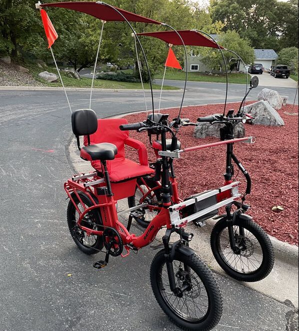 Bright Red Rattan eBikes paired next to each other to make a solid 4-wheel bicycle for two. Jump seat with armrests for an optional third rider.