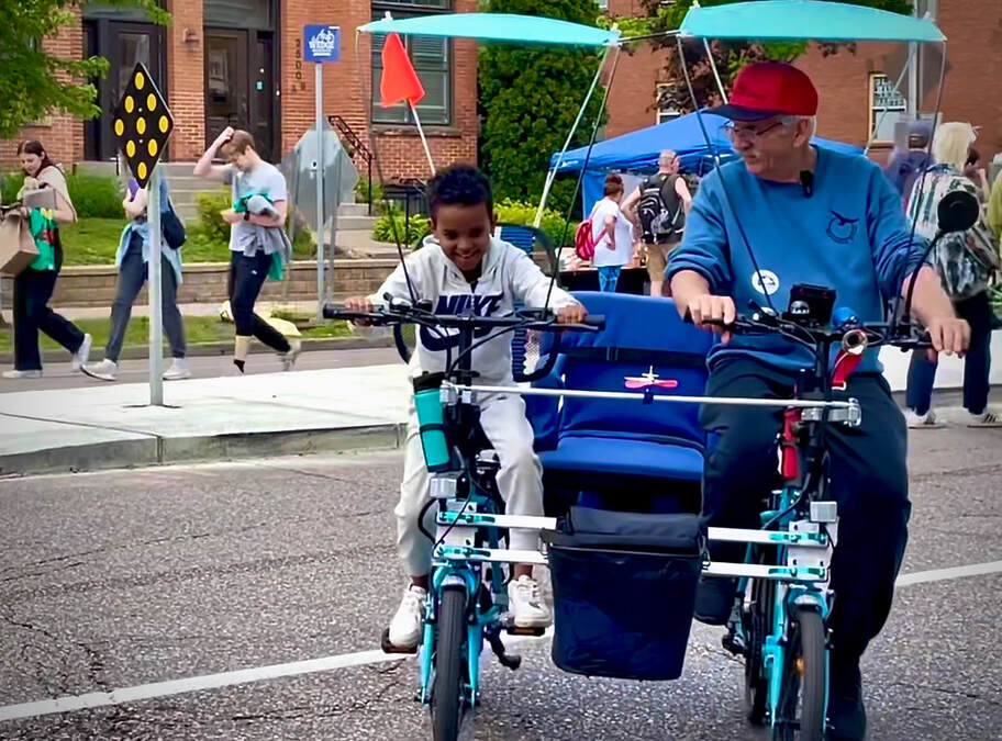 Jim enjoying a laugh with a young rider on a side-by-side sociable tandem bike at Lyndale Open Streets in Minneapolis Minnesota